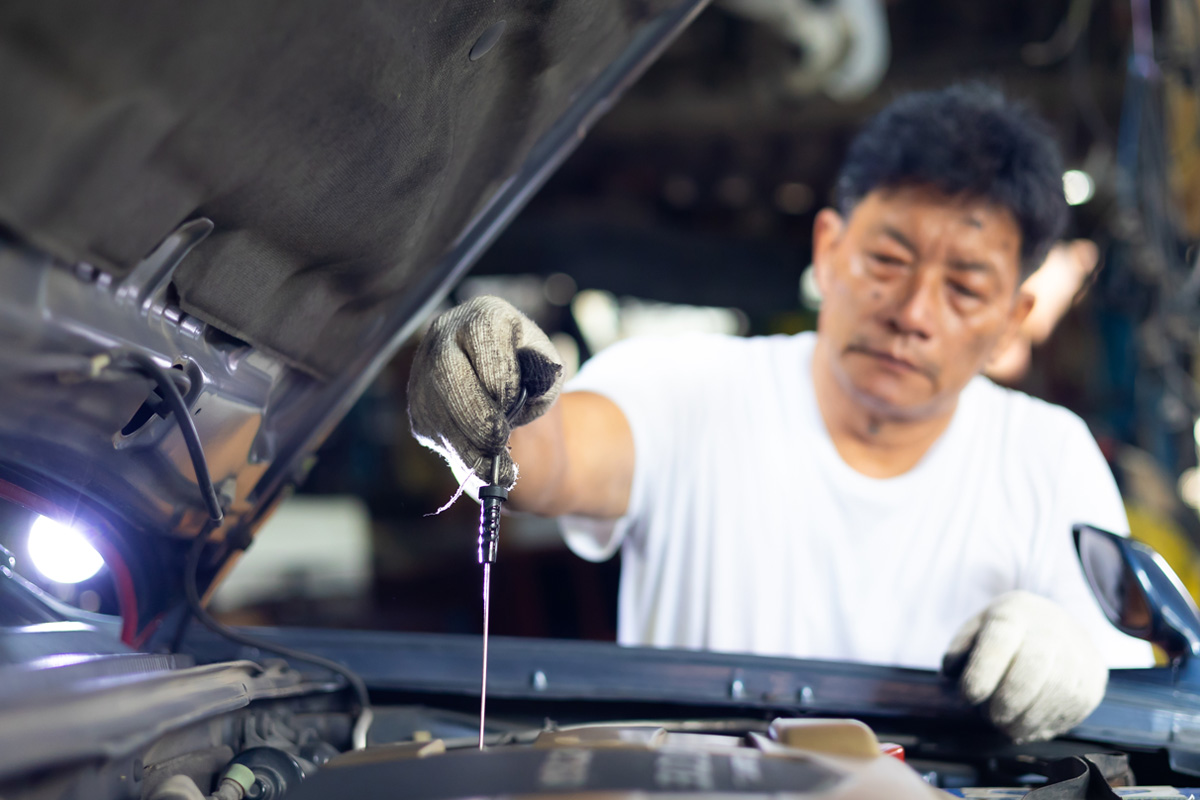 An asian man performing an engine oil dipstick check on a car engine.